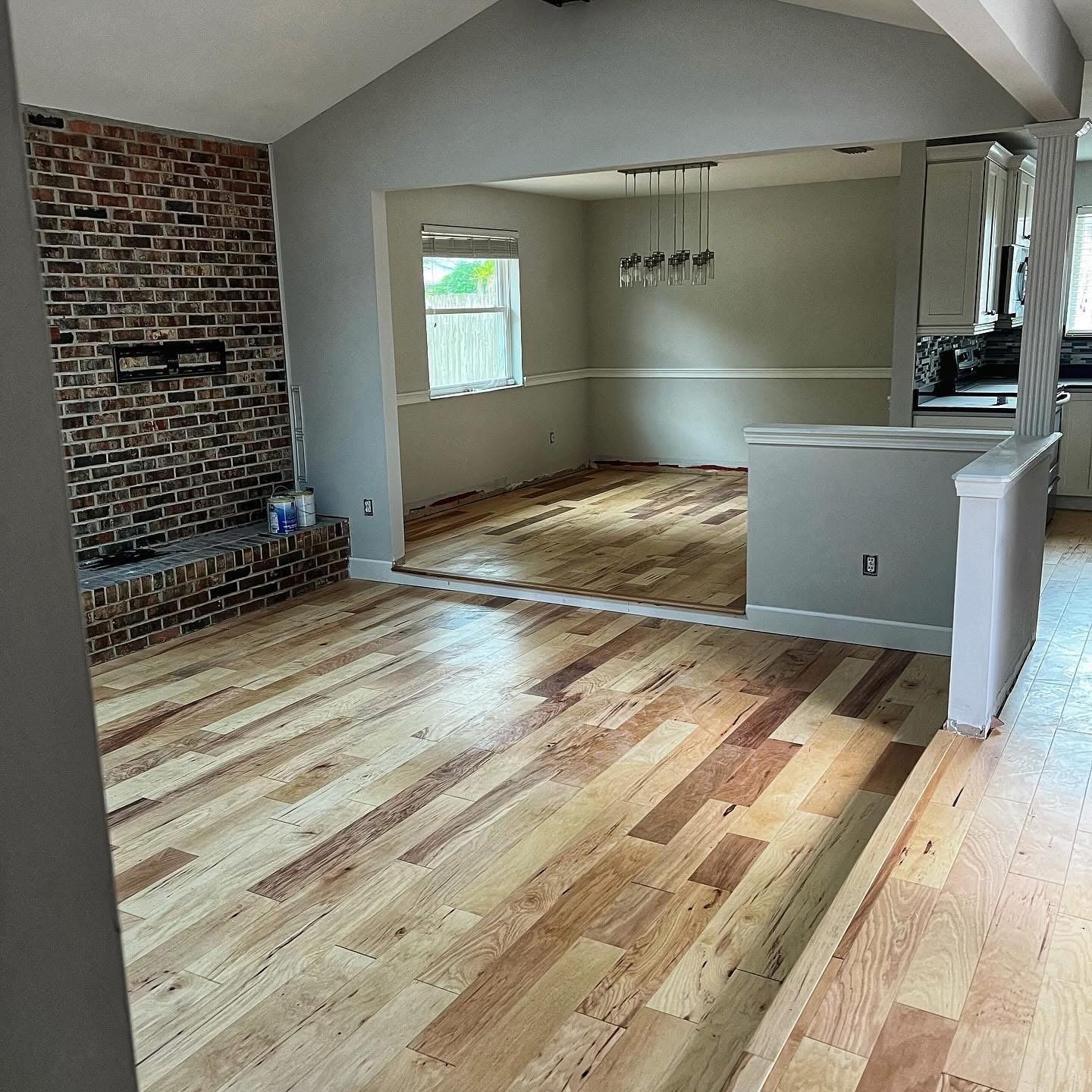 Open-concept living space with hardwood floors and brick accent wall